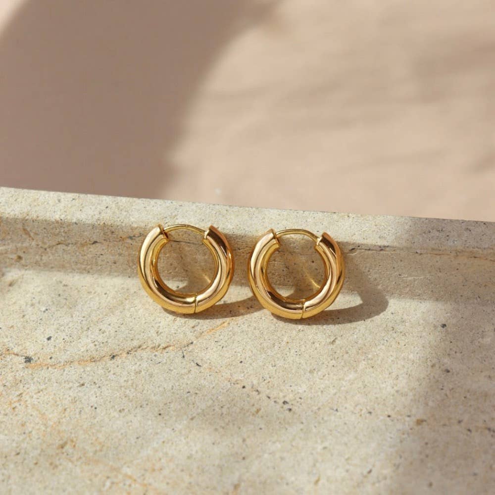 Chunky gold huggie hoop earrings displayed on a natural stone surface