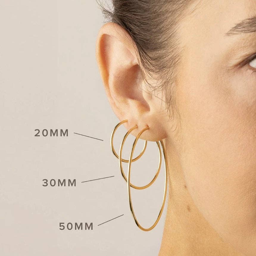 Close-up of a model wearing three different sizes of gold hoop earrings, labeled 20mm, 30mm, and 50mm to show size comparison.