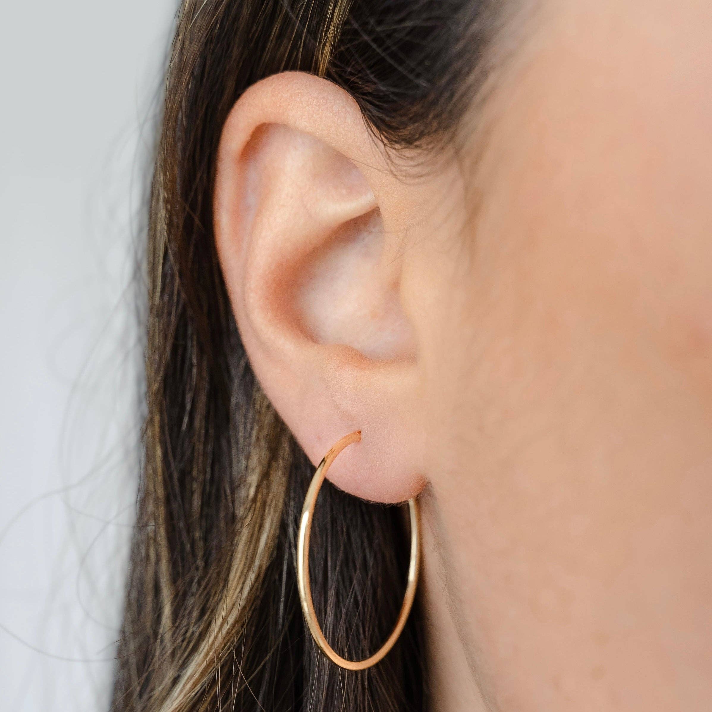 Close-up of a model wearing minimalist gold hoop earrings, highlighting their sleek and understated design on the ear.