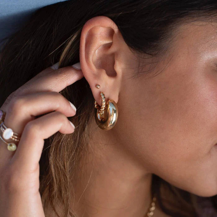 Close-up of a woman's ear wearing layered gold hoops, featuring a large statement hoop paired with a textured smaller hoop. The earrings highlight a trendy, stacked look perfect for everyday and bold style.