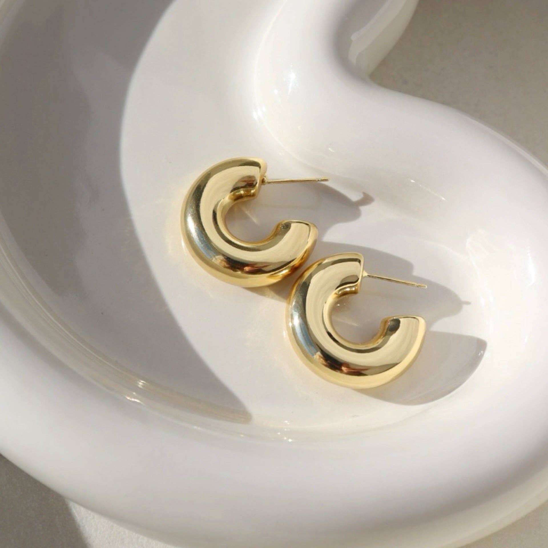 Chunky gold hoop earrings displayed on a modern white dish