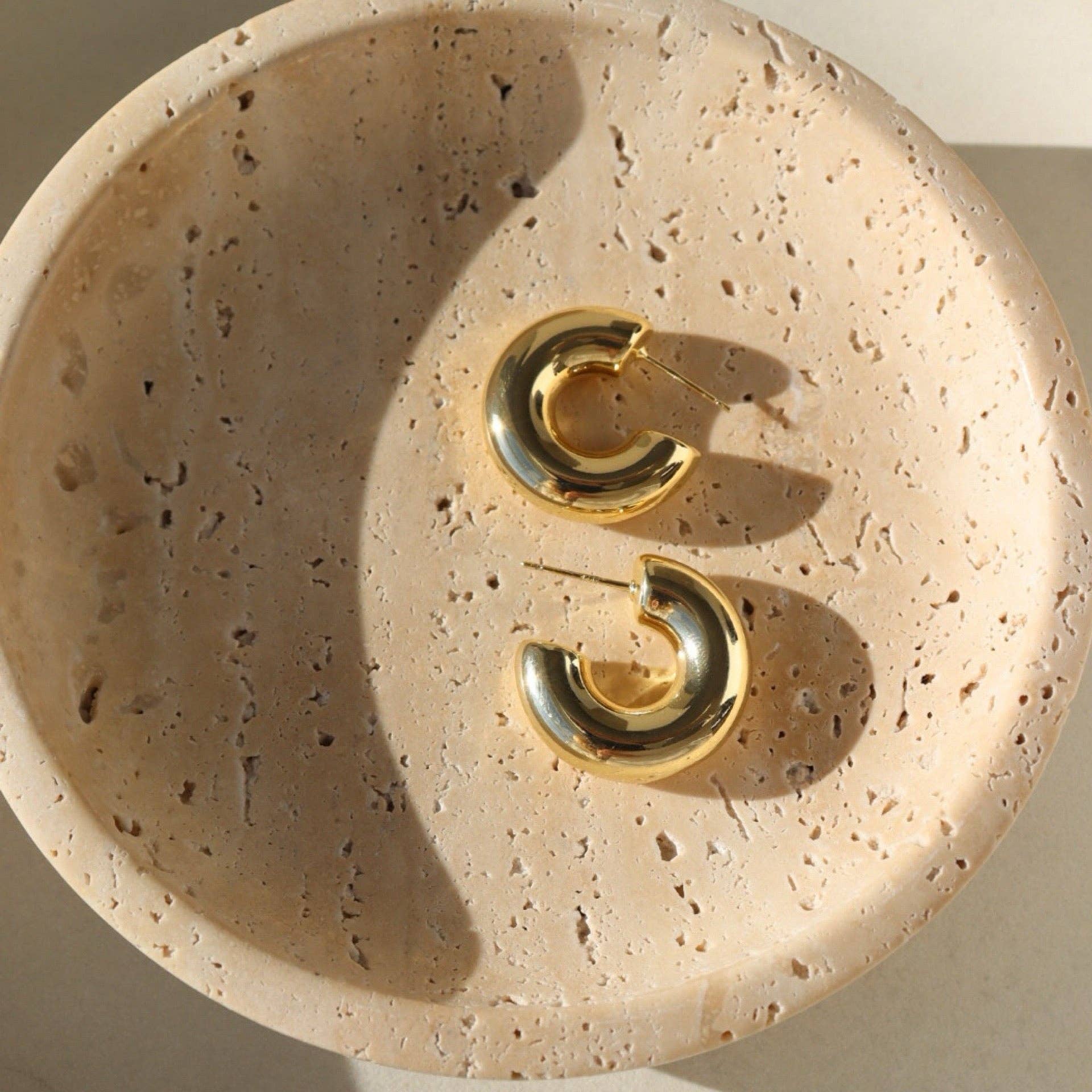 Chunky gold hoop earrings displayed on a textured stone dish