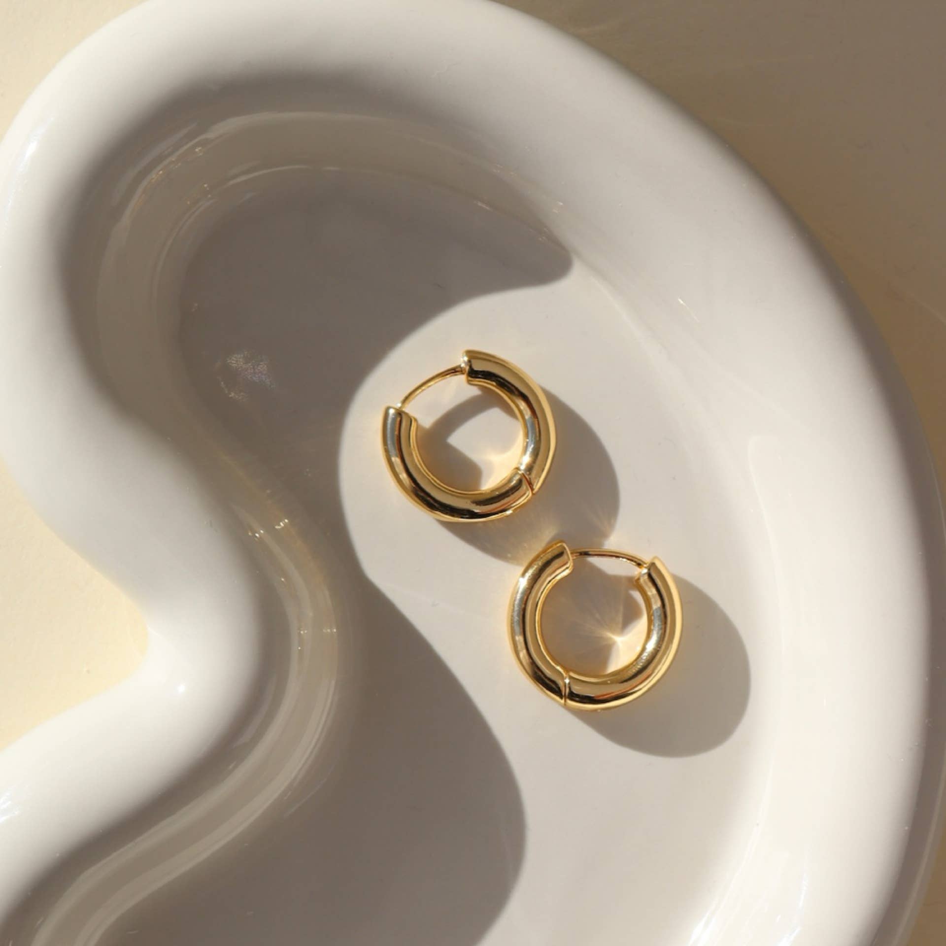 Chunky gold huggie hoop earrings displayed in a modern white dish