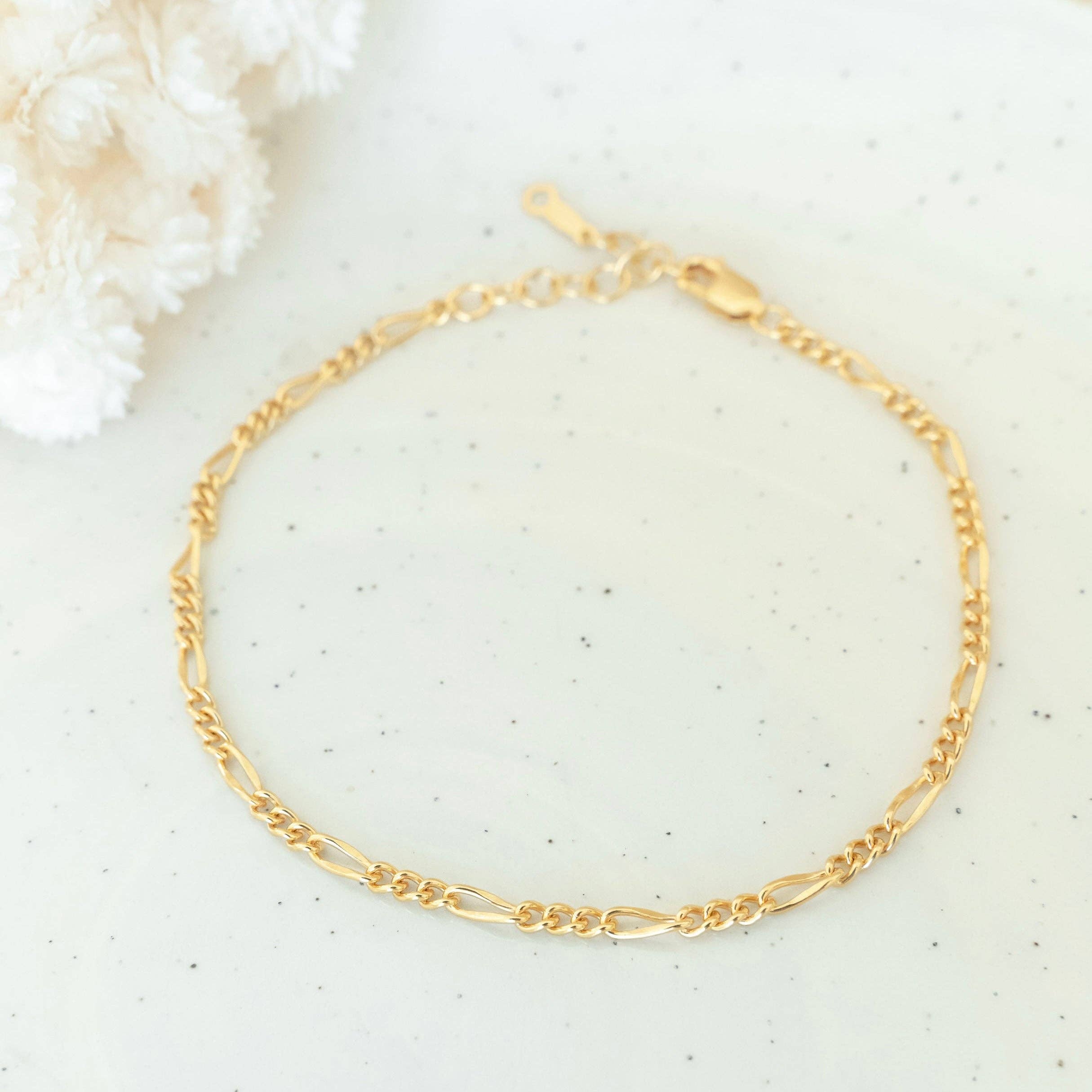 Delicate gold chain bracelet displayed on a white speckled surface