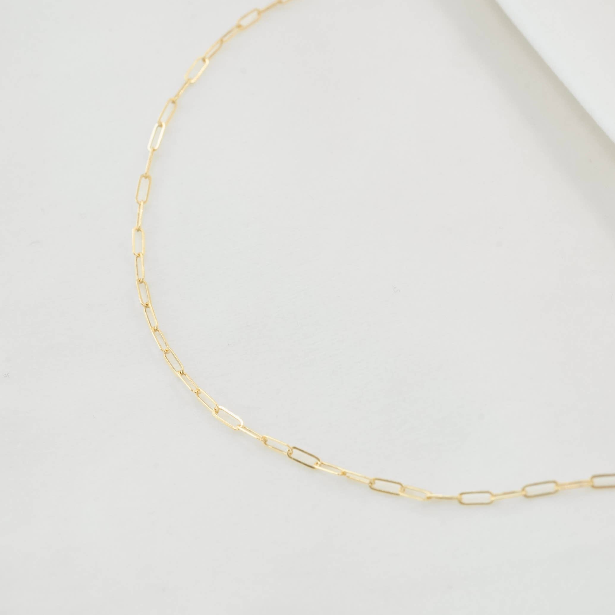 Delicate gold chain necklace with elongated links displayed against a clean white background, highlighting its minimalistic and modern design