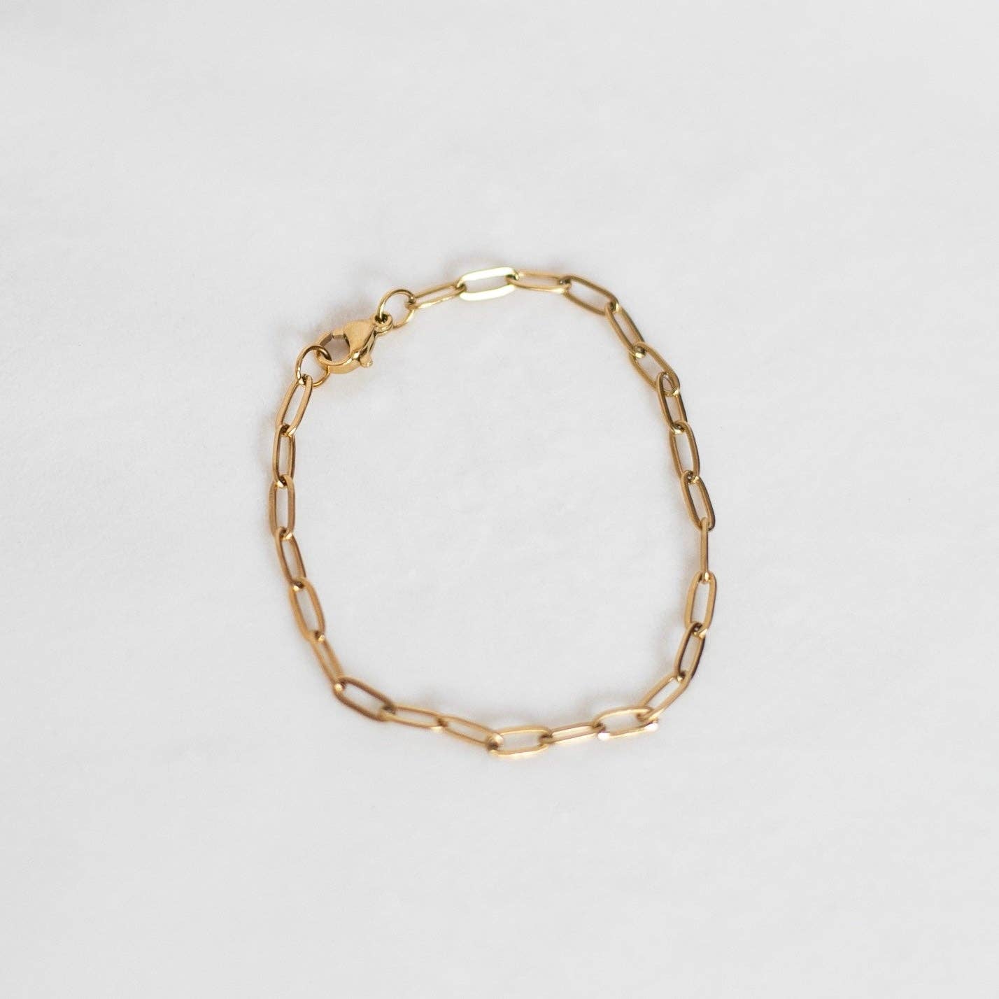 Delicate gold paperclip chain link bracelet on a white background