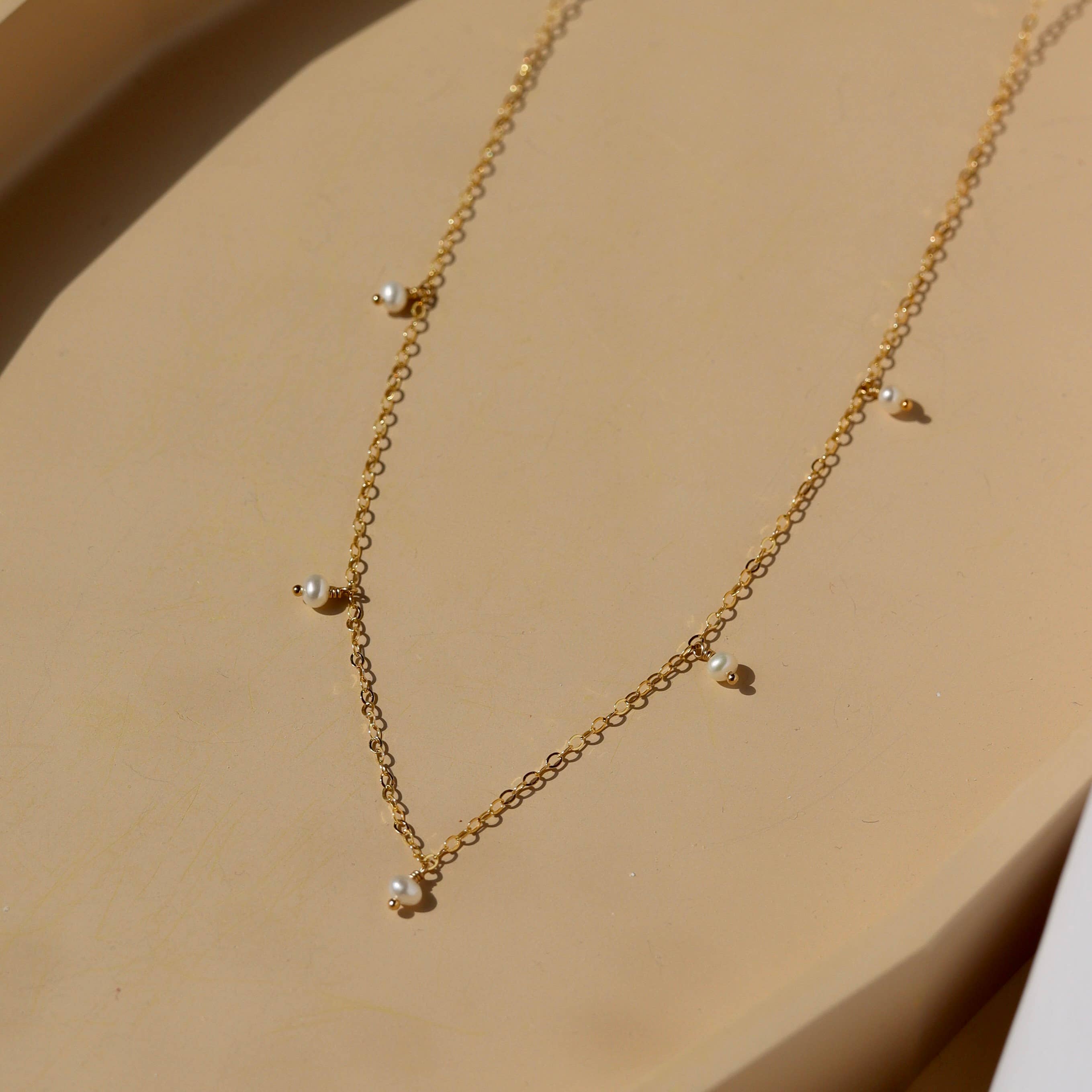 Delicate gold chain pearl necklace displayed on a soft beige surface