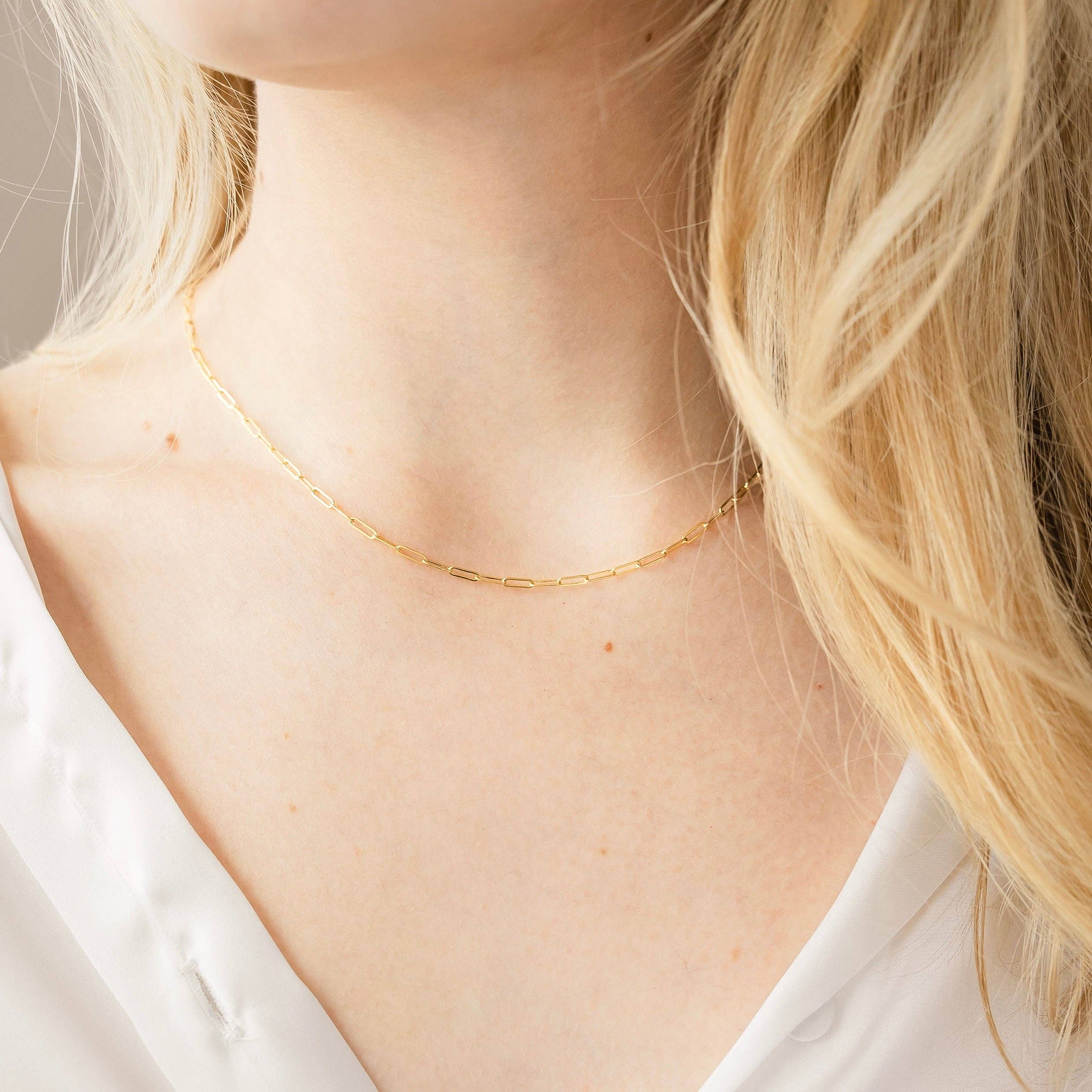 Model wearing a delicate gold chain necklace with elongated links, styled against a white shirt for a minimalistic and elegant look