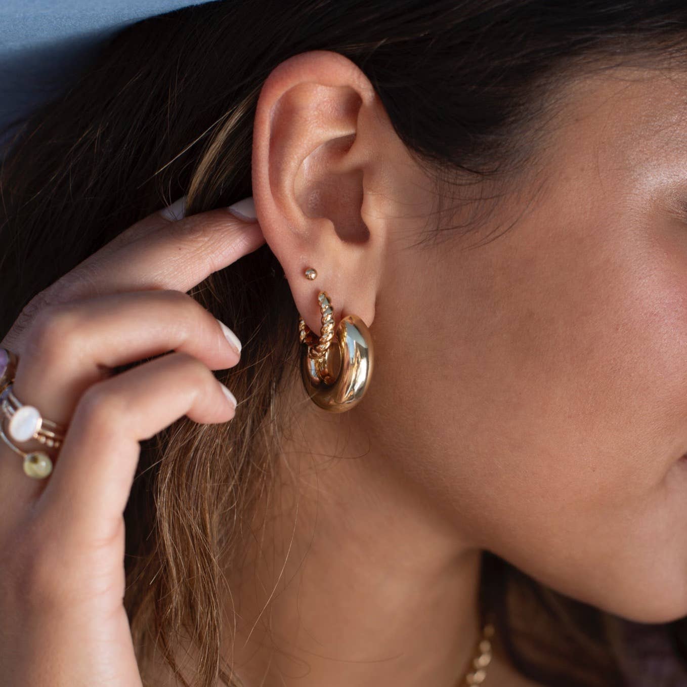 Gold croissant hoop earrings worn by a model, paired with additional gold jewelry