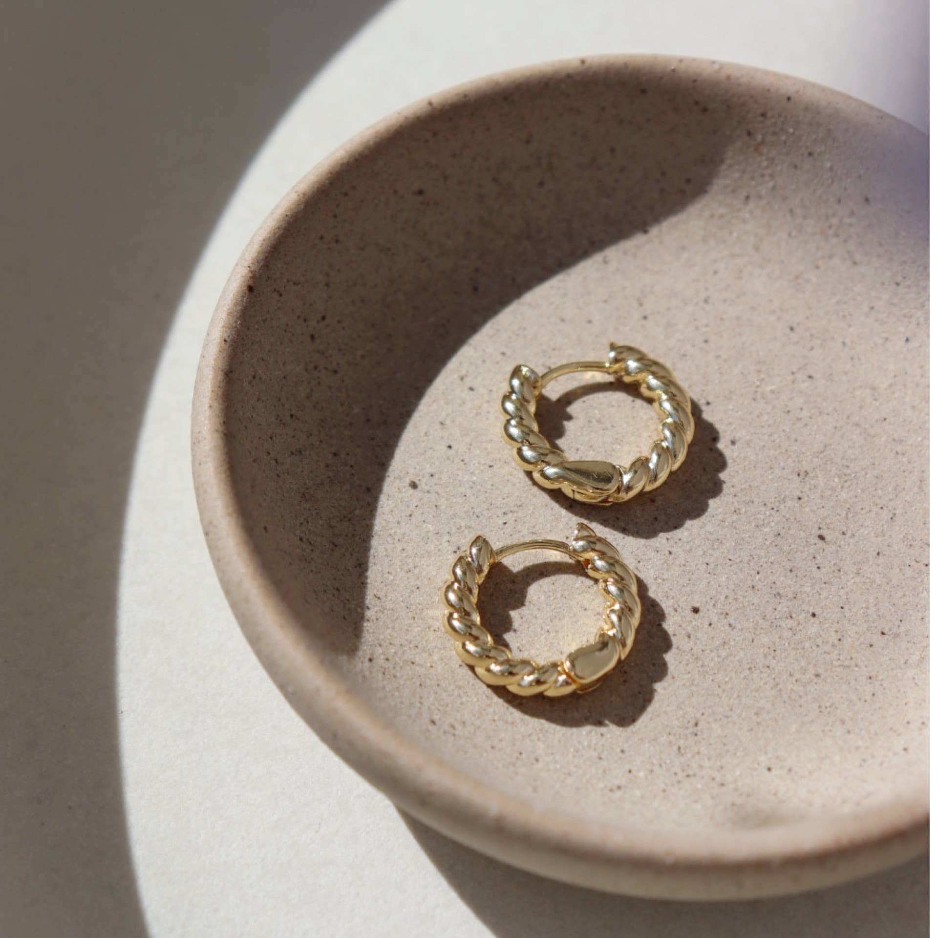 Gold croissant hoop earrings displayed in a textured stone bowl