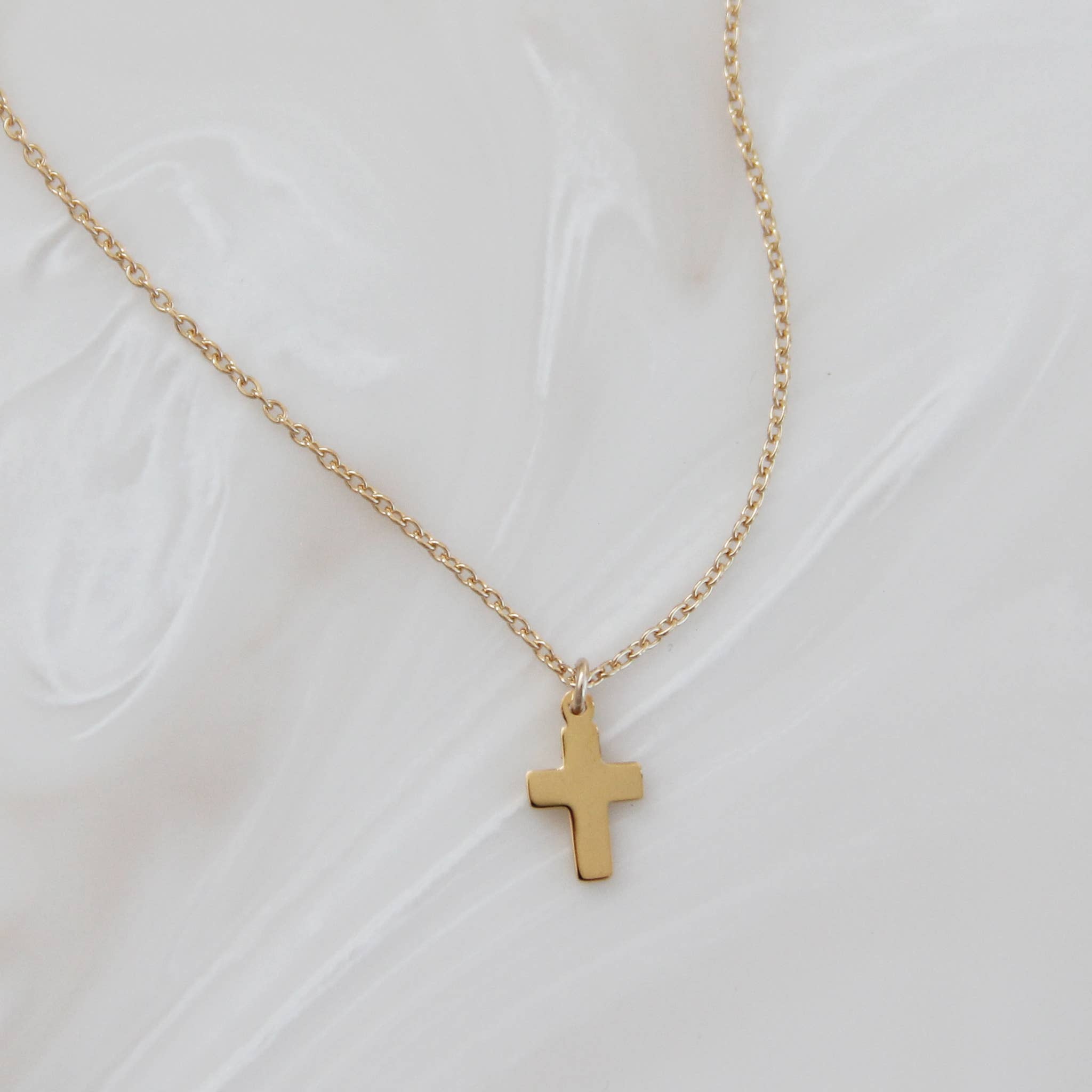 Gold cross pendant necklace displayed on a white marbled surface