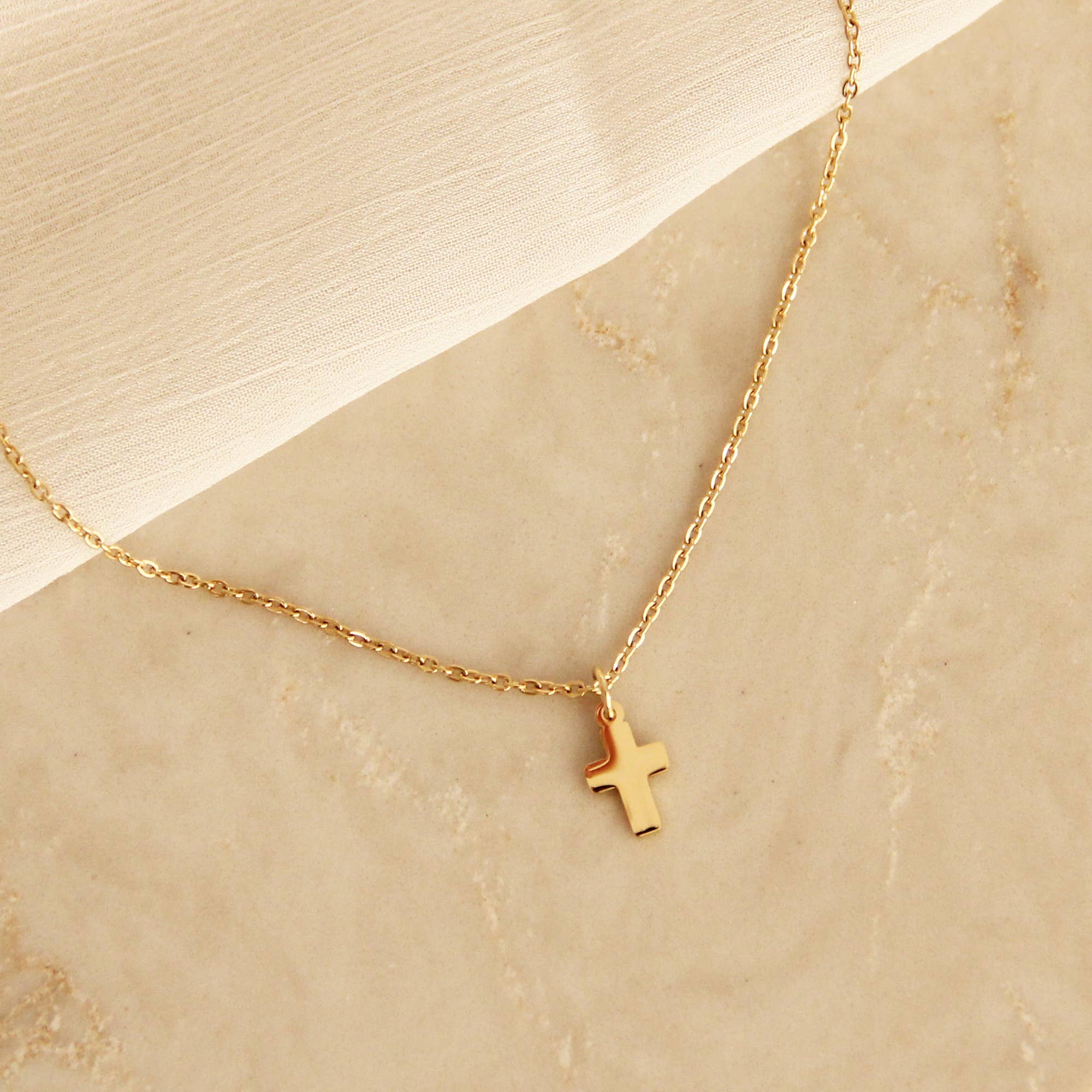 Gold cross pendant necklace displayed on a beige marble surface