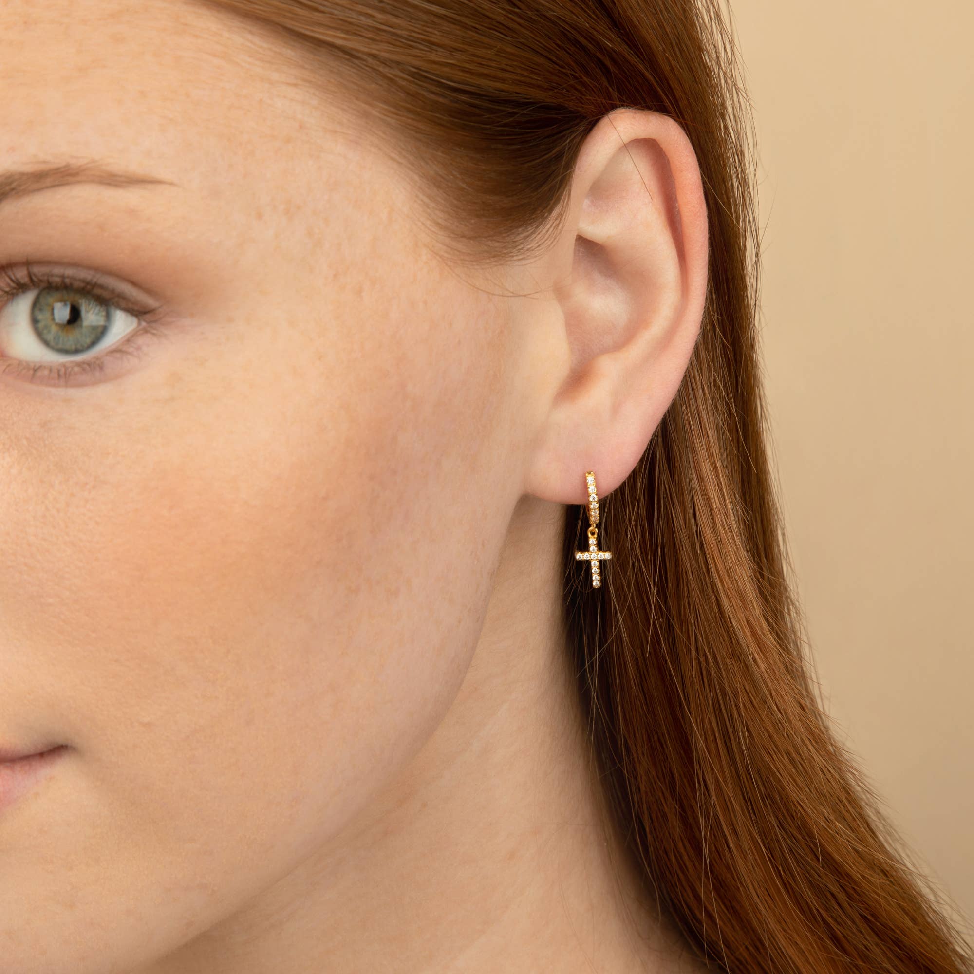 Model wearing delicate gold hoop earrings with a cubic zirconia cross pendant