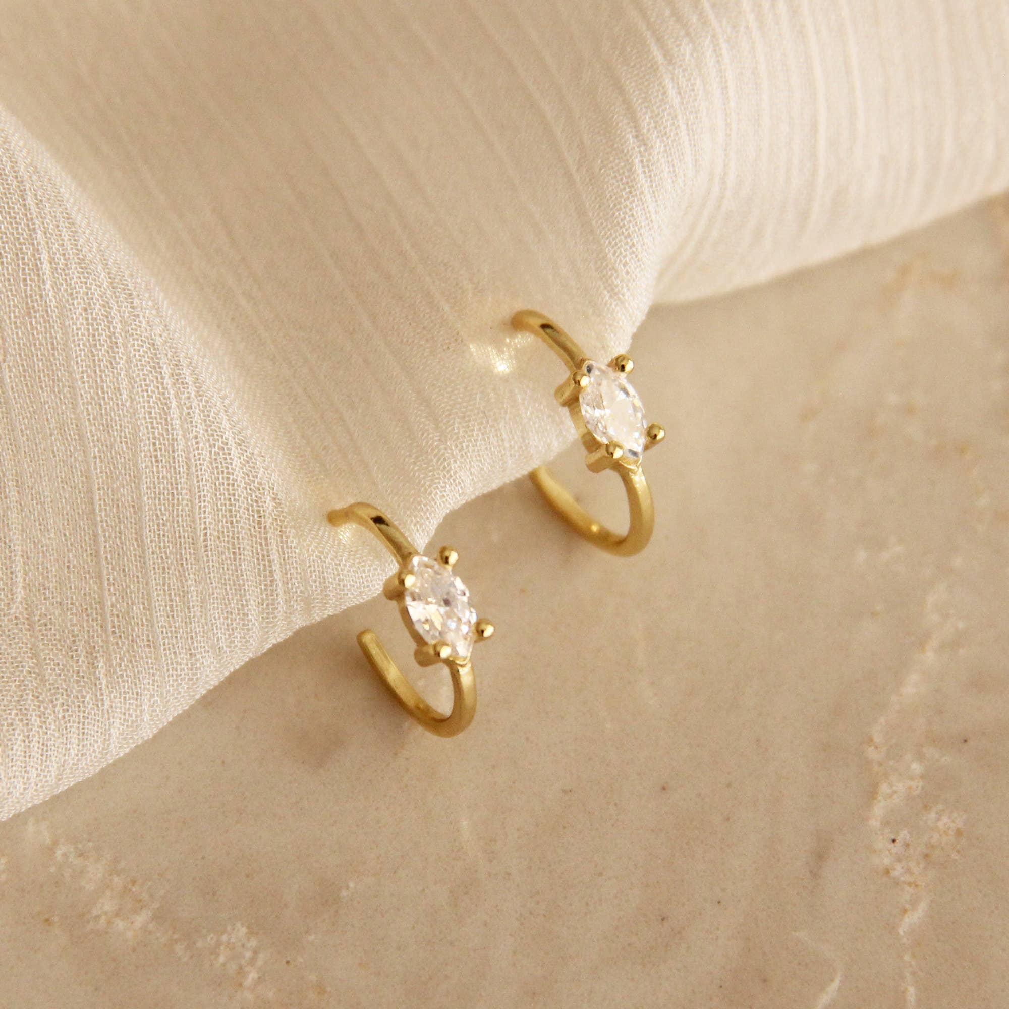 Gold hoop earrings with marquise cut cubic zirconia stones on a soft fabric background