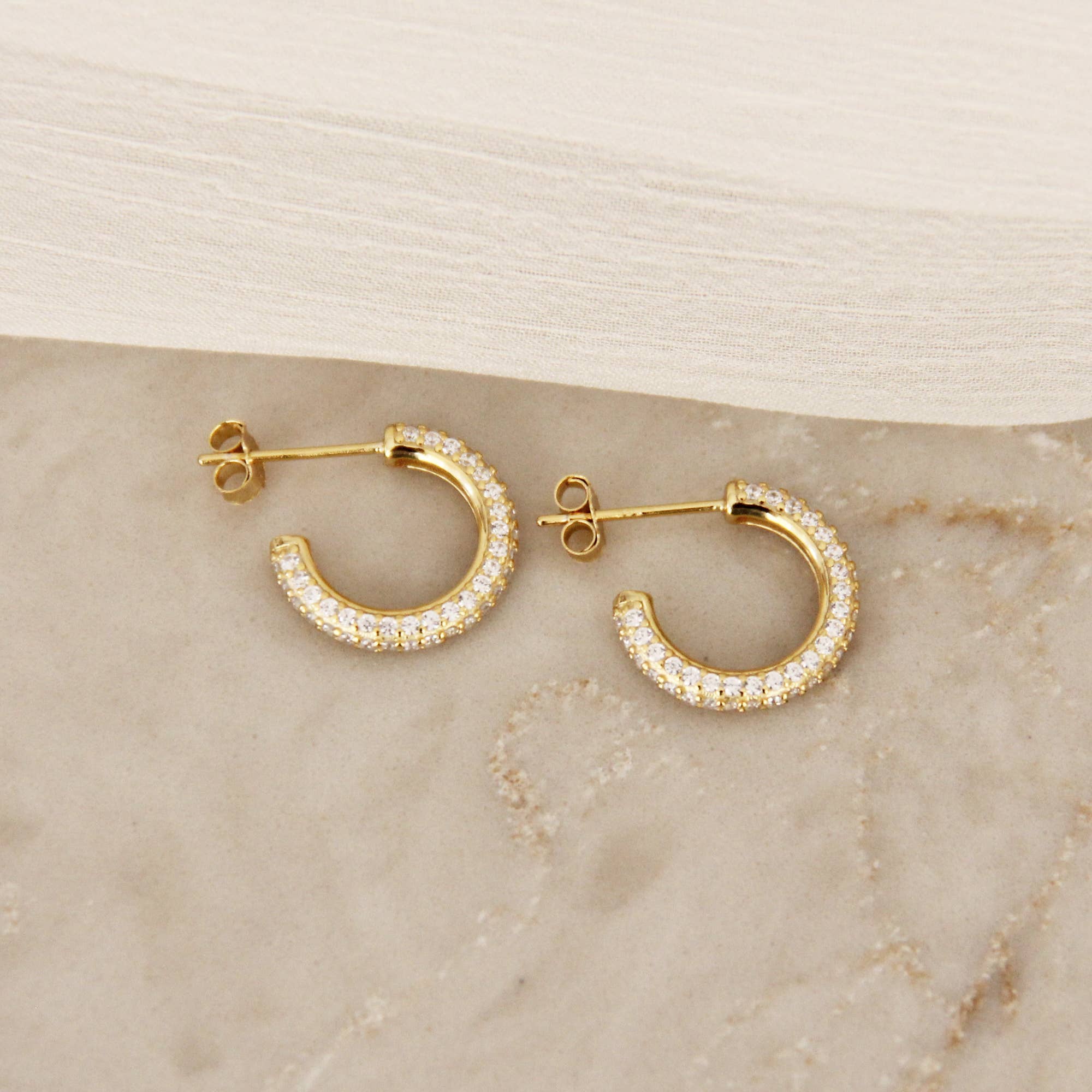 Gold pavé hoop earrings encrusted with cubic zirconia stones displayed on a marble surface