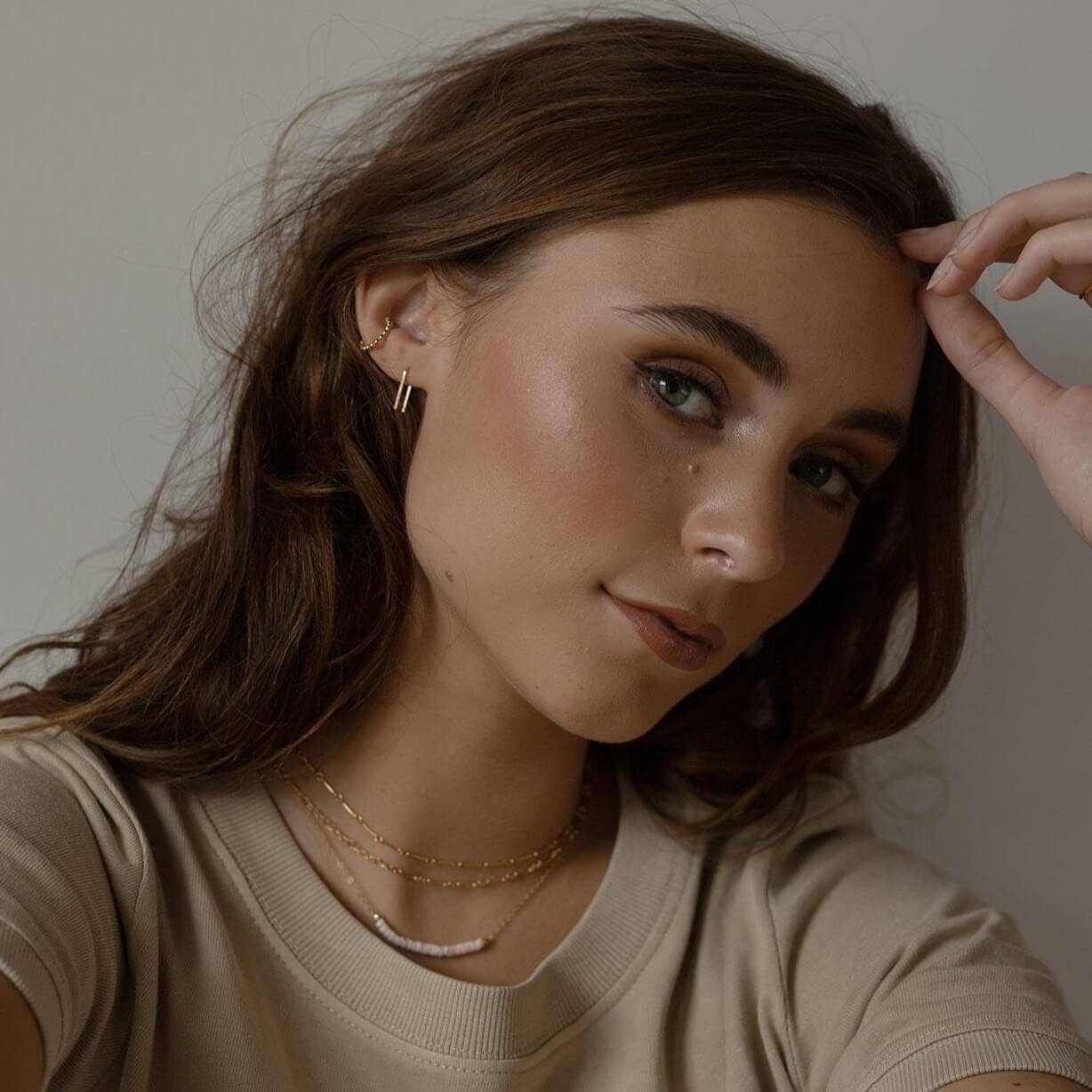 Model wearing minimalist gold staple earrings paired with layered necklaces, highlighting a chic, understated style