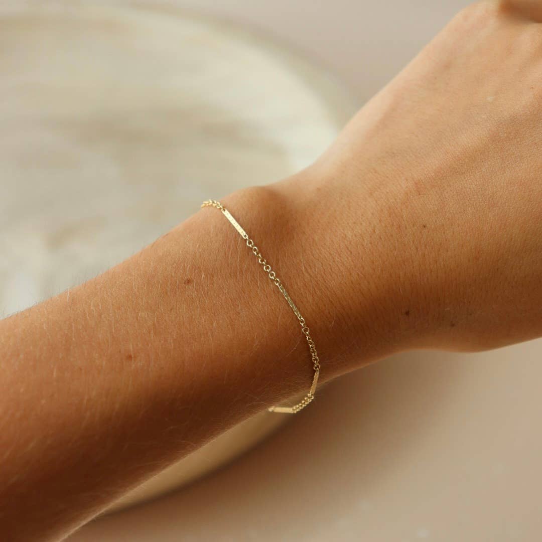 Gold bracelet with alternating textured and smooth chain links worn on the wrist, shown in natural lighting.