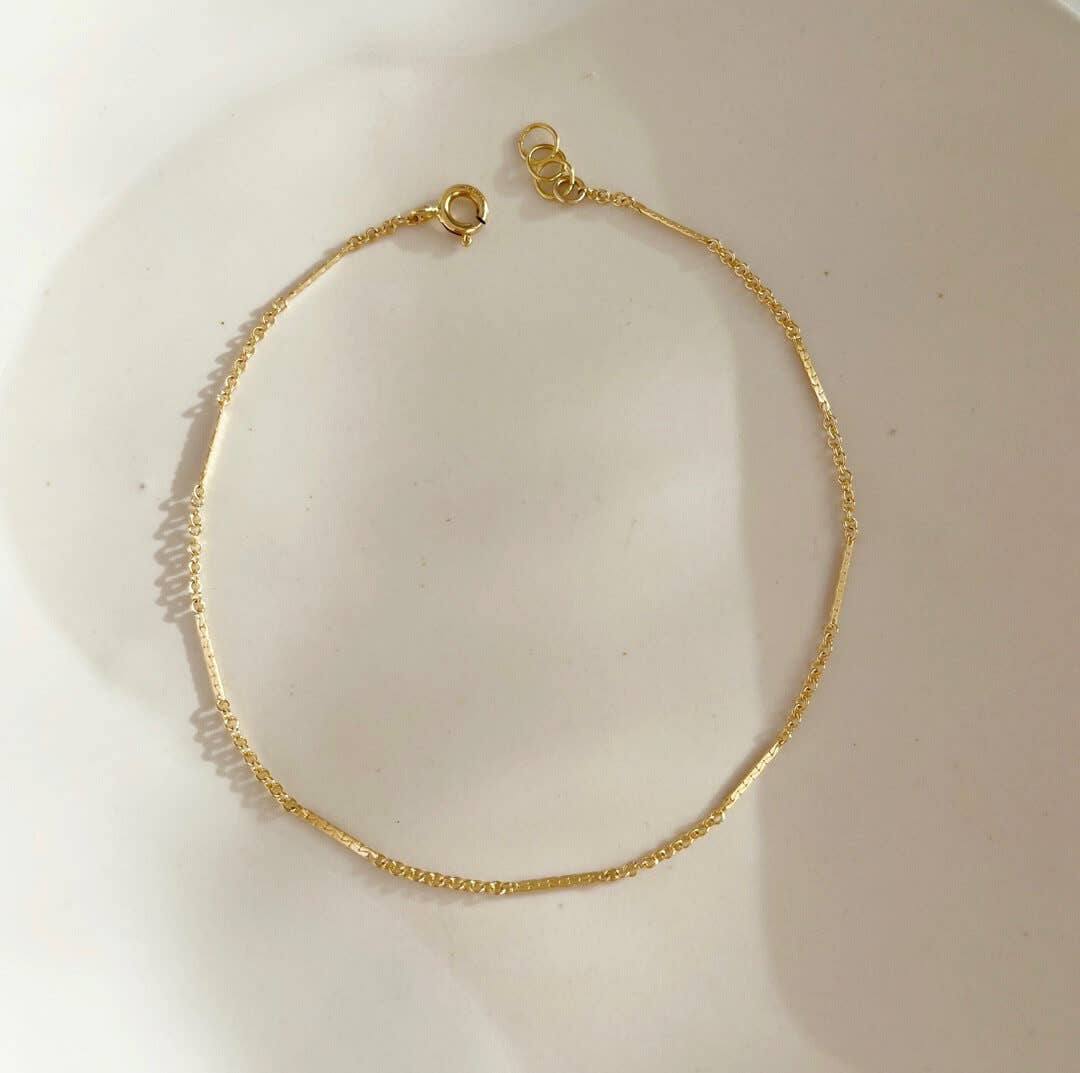 Delicate gold bracelet with alternating textured and smooth chain segments, displayed flat on a neutral background.