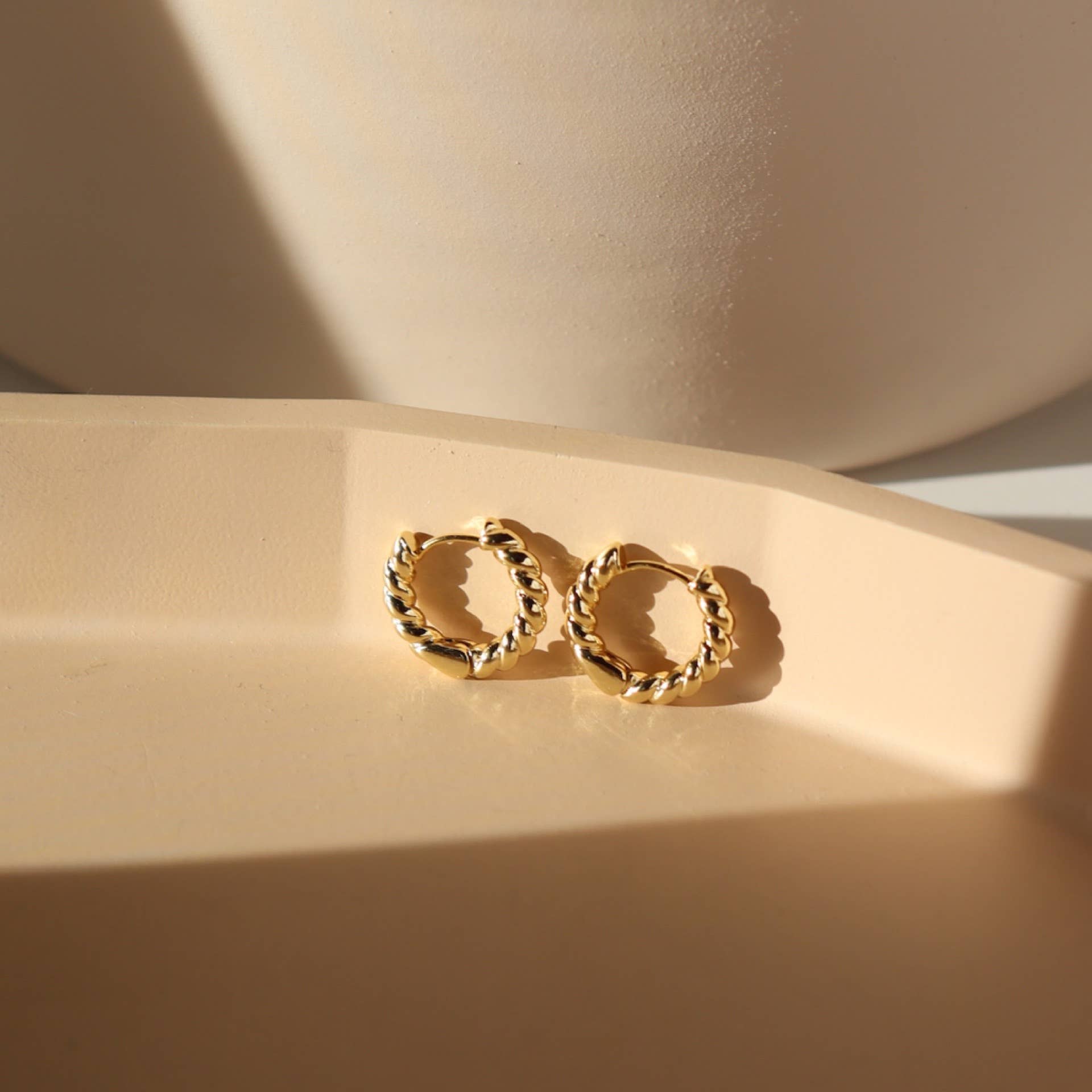 Gold twisted rope hoop earrings displayed on a geometric beige surface