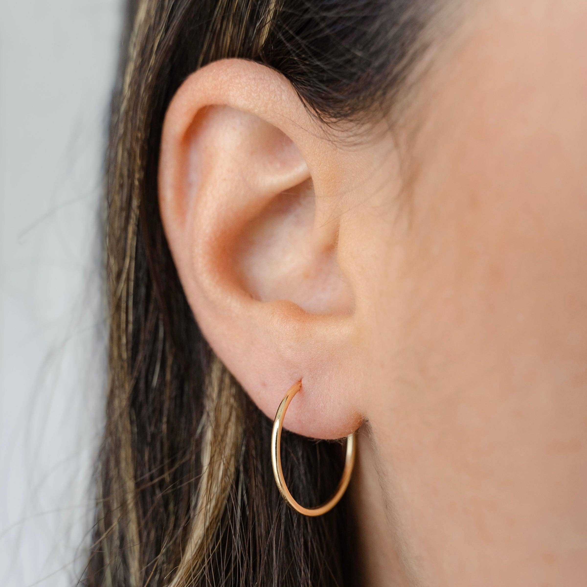 Close-up of a model wearing minimalist gold hoop earrings, highlighting their sleek and understated design on the ear.