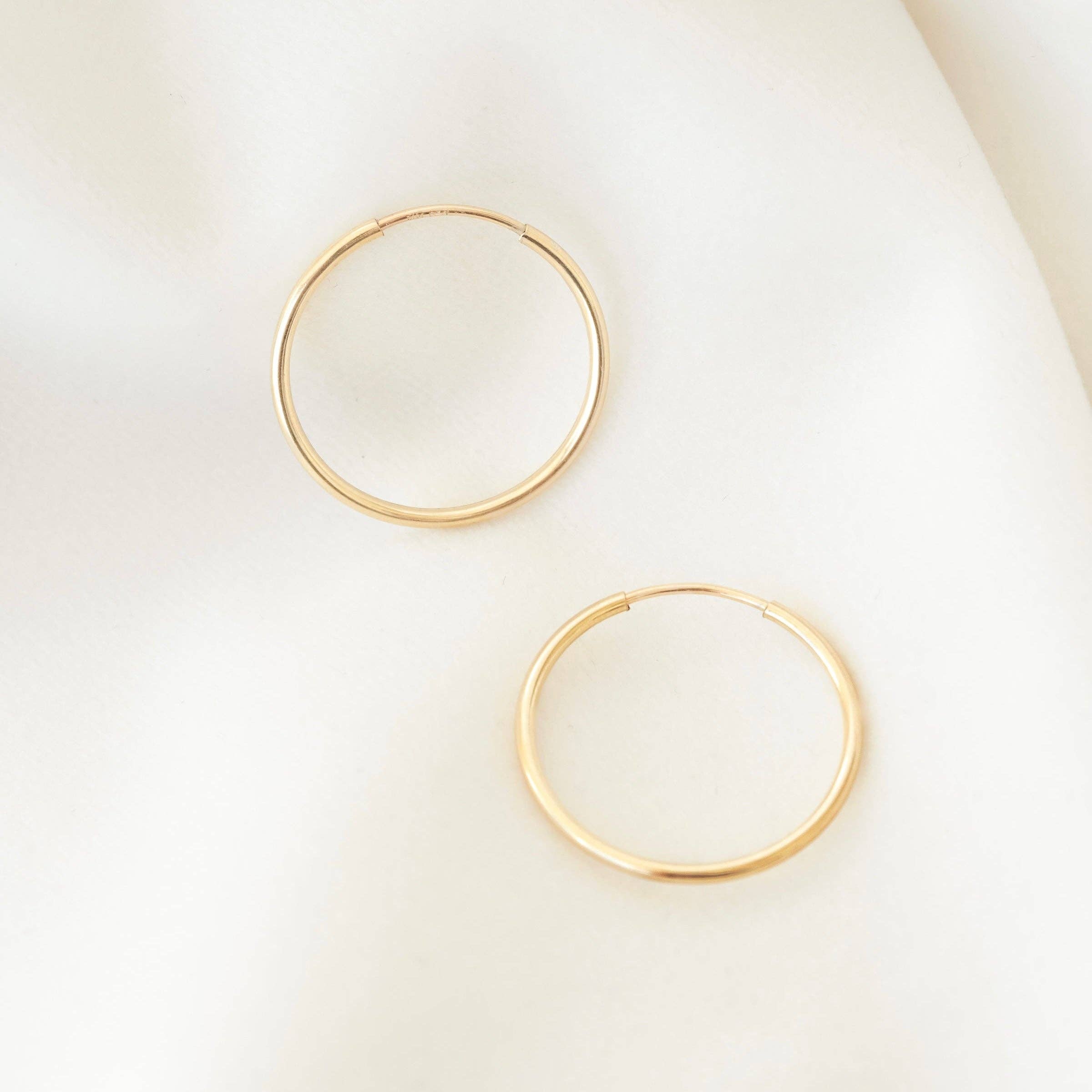 A pair of minimalist gold hoop earrings laid on a soft white fabric, showcasing their sleek and simple design