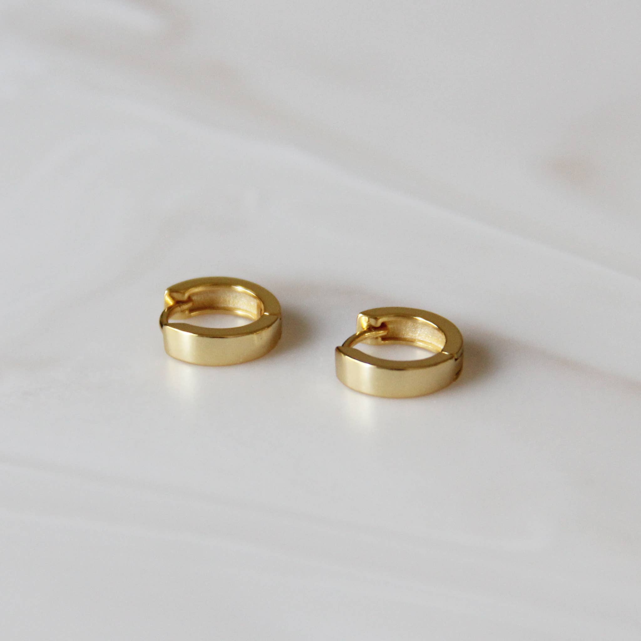 Minimalist gold huggie hoop earrings angled on a white surface