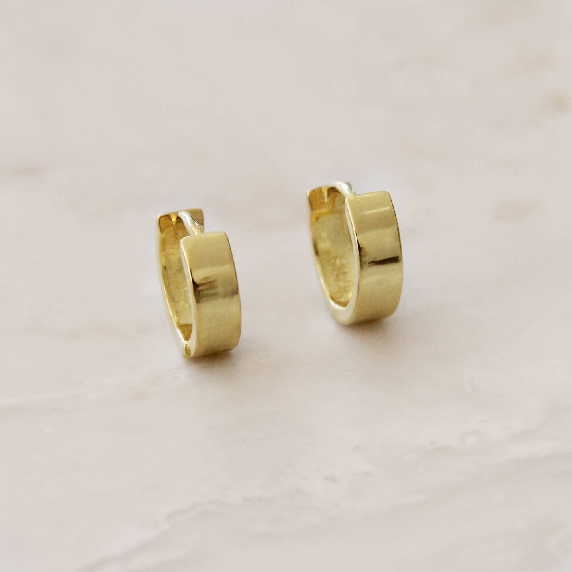 Minimalist gold huggie hoop earrings on a marble surface