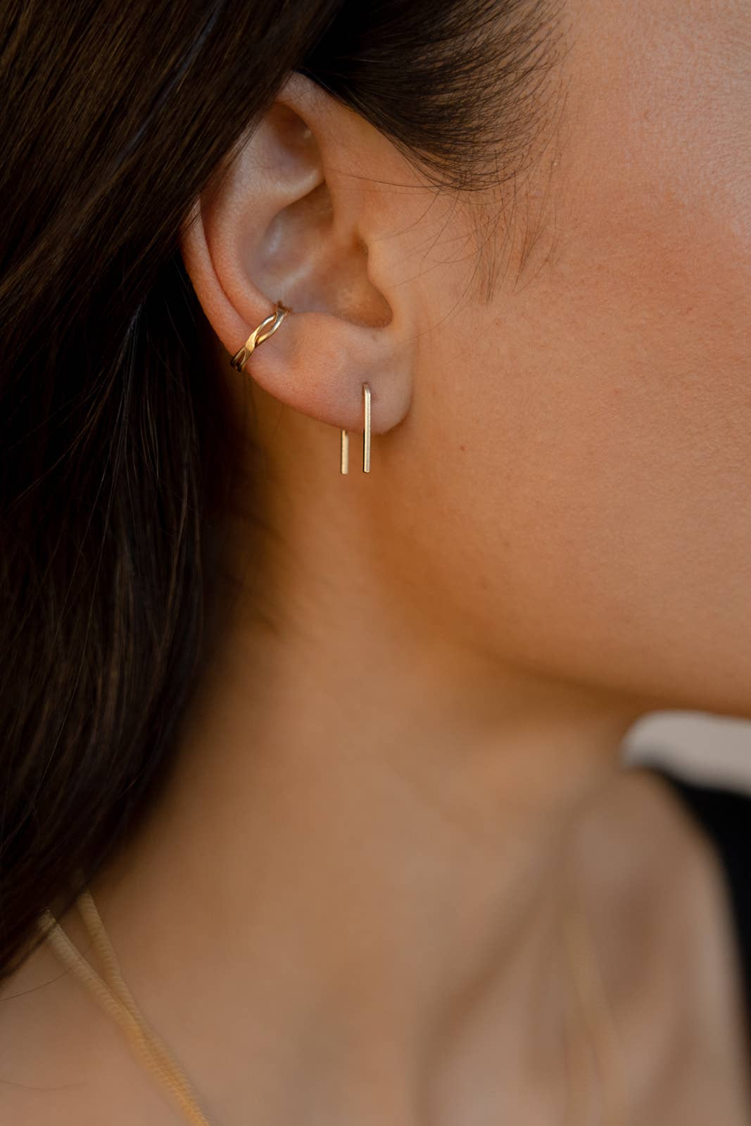 Gold rectangular staple earrings worn by a model, showcasing their sleek and minimalist design with a second hoop earring for a layered, contemporary look