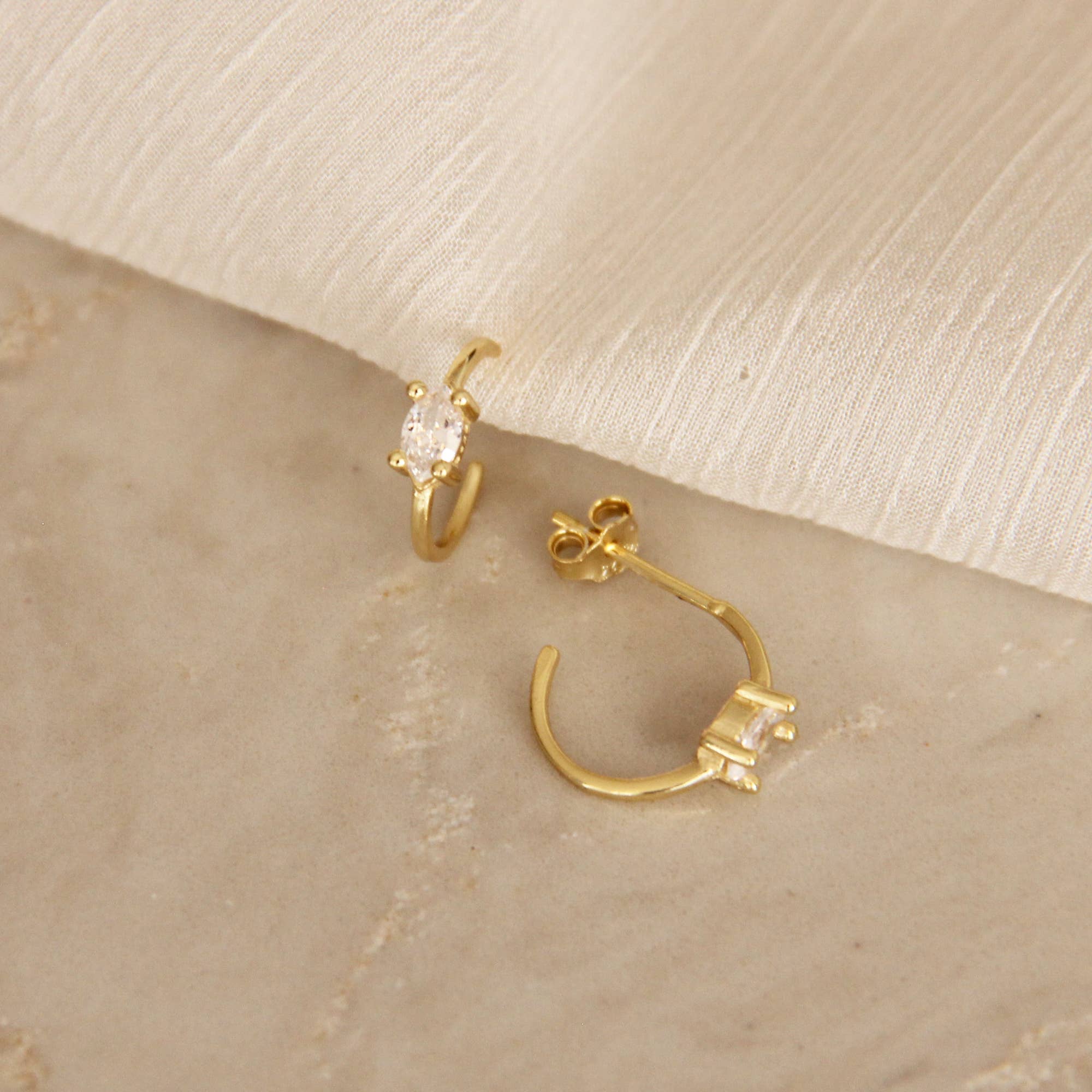 Gold hoop earrings with marquise cut cubic zirconia stones displayed on a marble surface