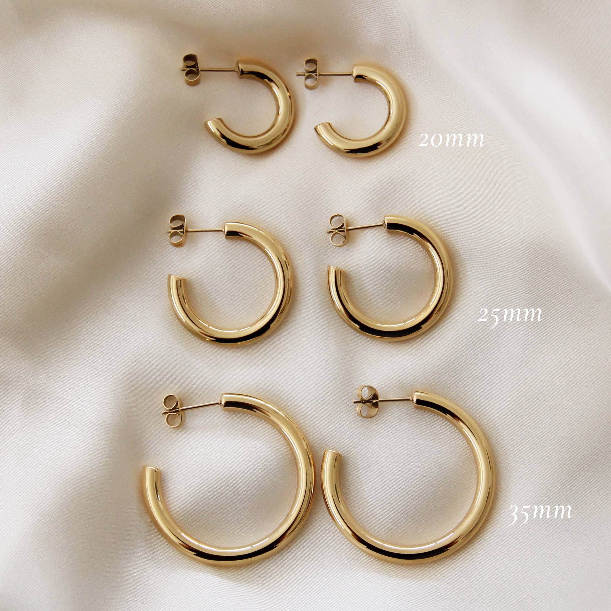 Set of gold hoop earrings in 20mm, 25mm, and 35mm sizes displayed on soft white fabric