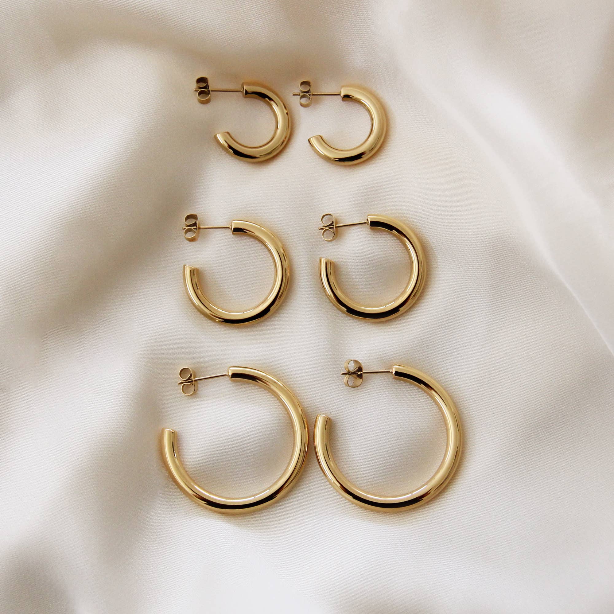 Set of gold hoop earrings in various sizes displayed on a soft white fabric