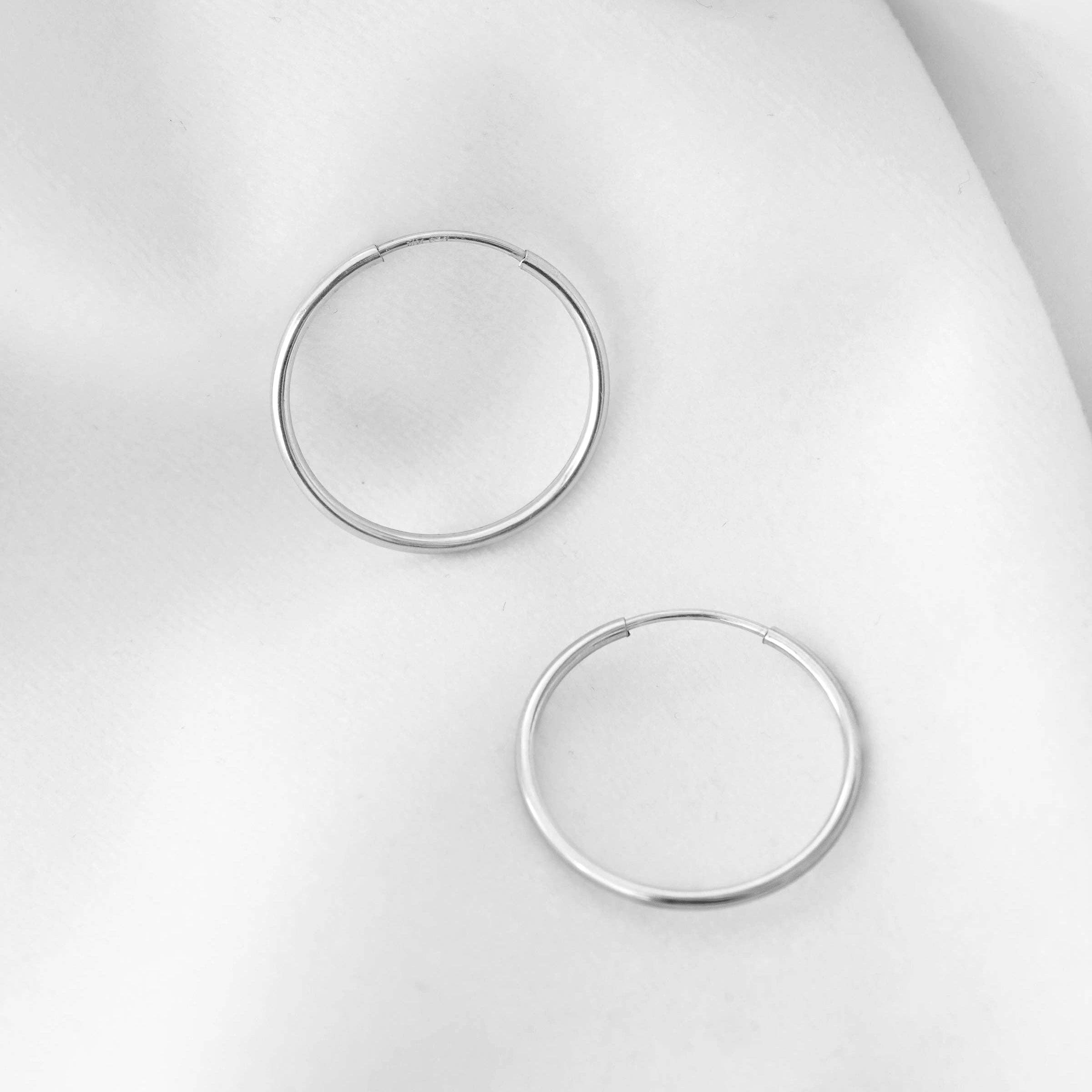 Sterling silver hoop earrings displayed on a soft white fabric background