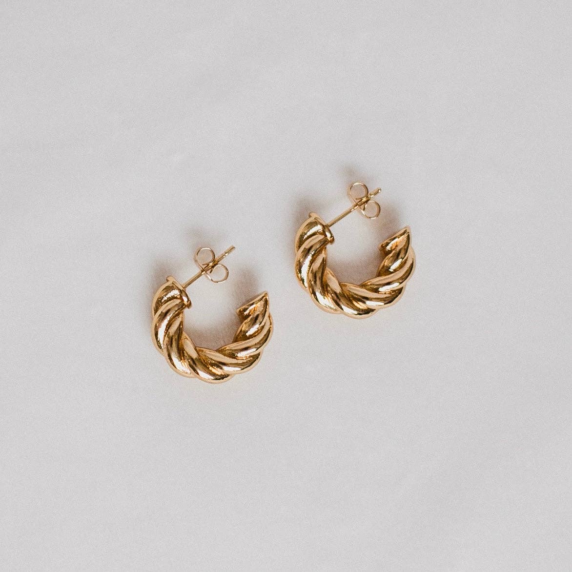 Twisted gold hoop earrings displayed against a light background, showcasing their textured design and elegant finish.